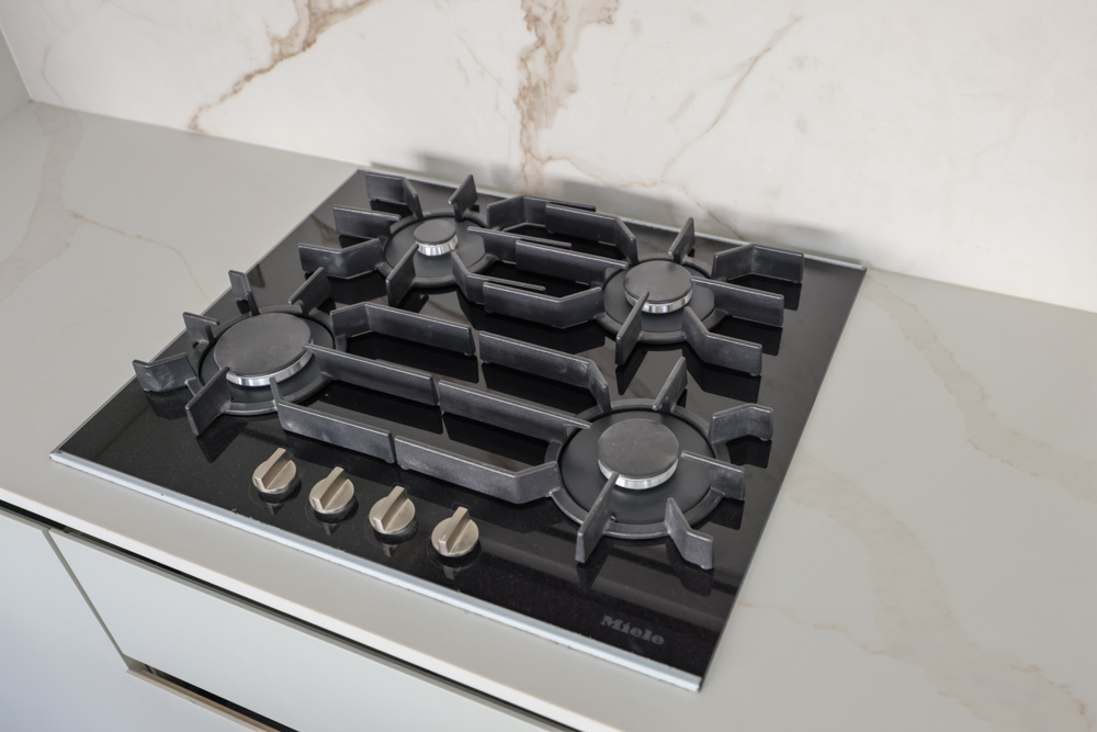 Beach Walk Residence A black gas cooktop with four burners and control knobs, set on a sleek, light-colored countertop.
