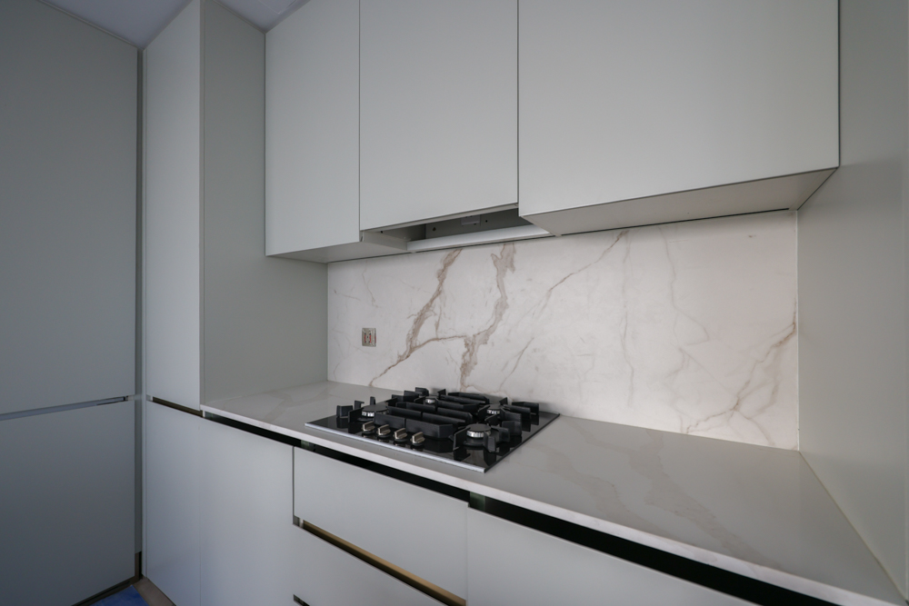 Beach Walk Residence Modern kitchen with sleek cabinets, a gas stove, and a marble backsplash, creating a clean, minimalist design.