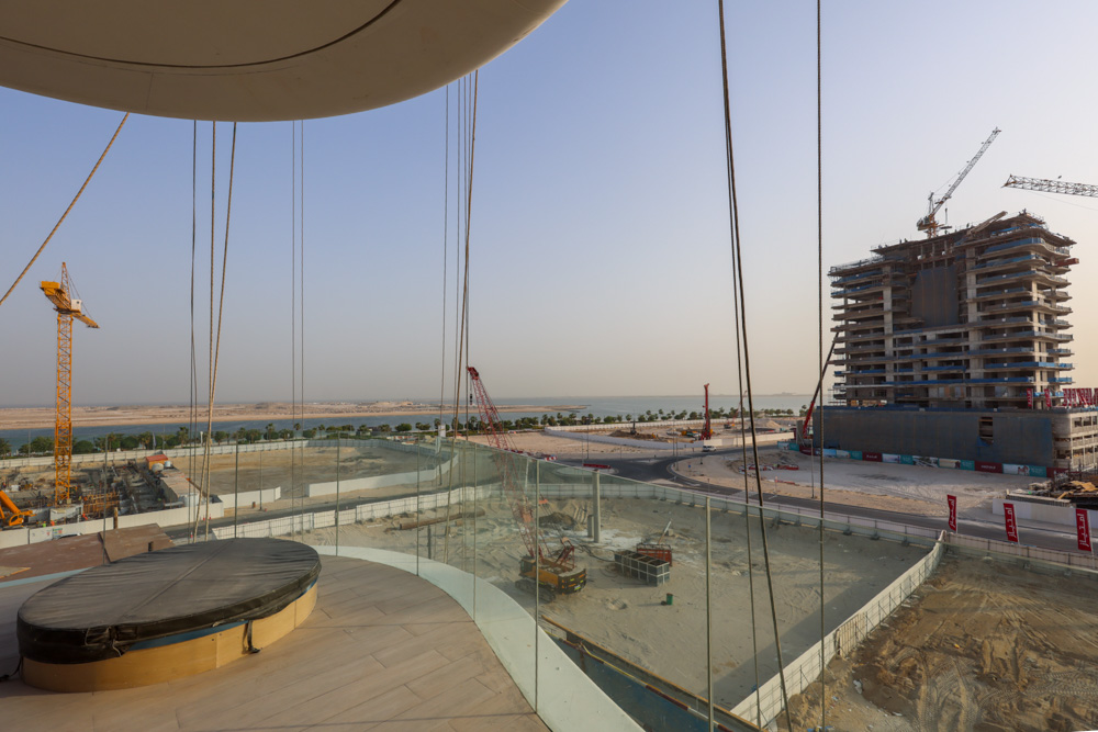 Beach Walk Residence View from a glass balcony showing a construction site with cranes and progressing buildings against a clear sky.