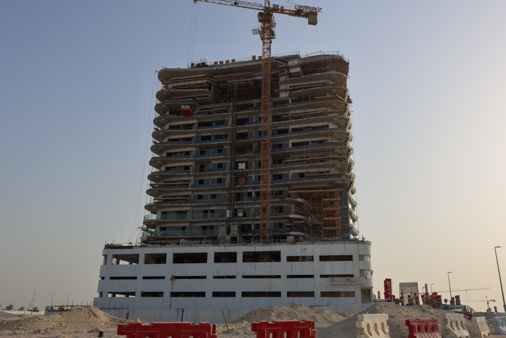 Beach Walk Residence A tall building under construction with scaffolding, a crane, and surrounding construction materials in a clear sky.