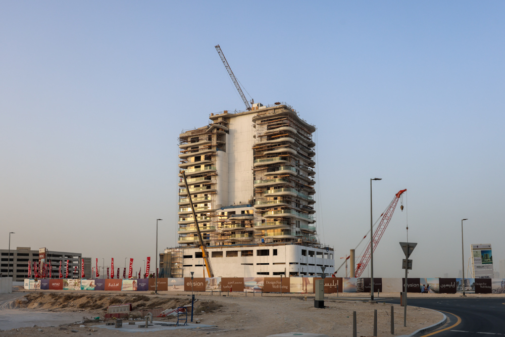 Beach Walk Iii By Imtiaz A partially constructed high-rise building with scaffolding, cranes, and construction signs in a desert environment.