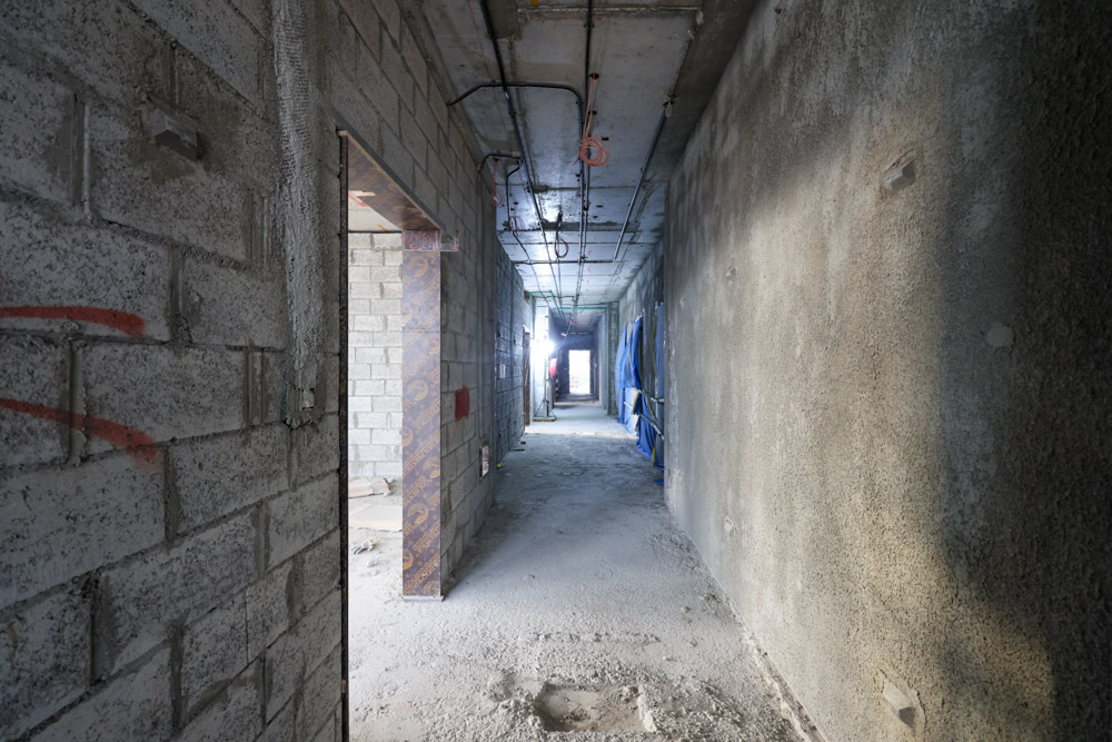 Beach Walk Iii By Imtiaz Long, unfinished hallway with bare walls, exposed wiring, and construction materials. Light visible at the far end.