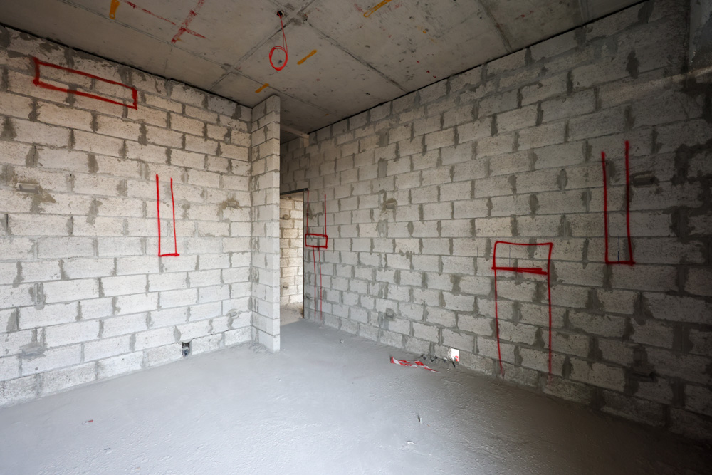 Beach Walk Iii By Imtiaz An unfinished room with exposed concrete block walls, marked with red lines, and a plain floor.