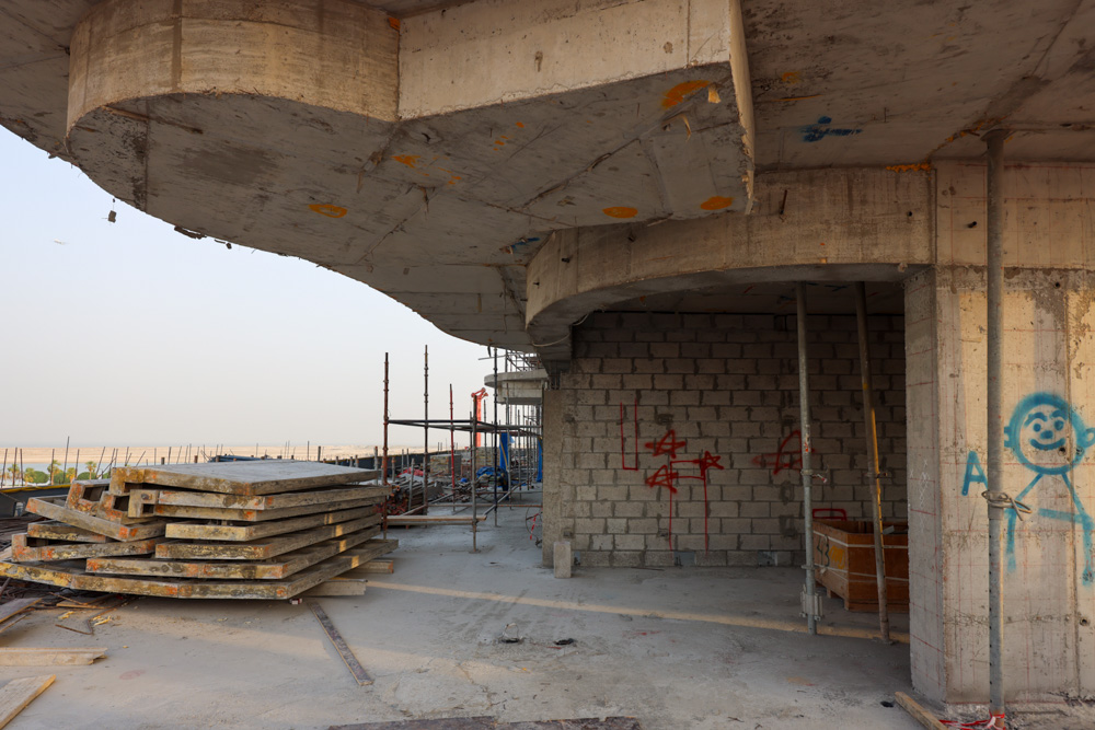 Beach Walk Iii By Imtiaz A construction site featuring concrete structures, stacked slabs, scaffolding, and graffiti on the walls.