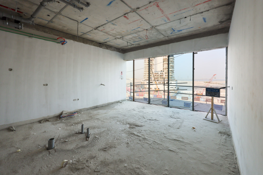 Beach Walk Iii By Imtiaz An unfinished room with bare walls, exposed pipes, and a large window overlooking a construction site.