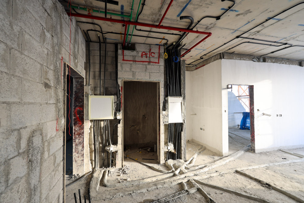 Beach Walk Iii By Imtiaz Construction site interior featuring exposed wiring, unfinished walls, and electrical panels. Dusty floor and pipes visible.