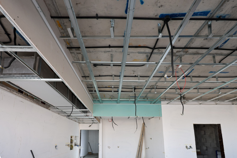 Beach Walk Iii By Imtiaz An unfinished ceiling with exposed metal framework and electrical wiring in a partially constructed room.