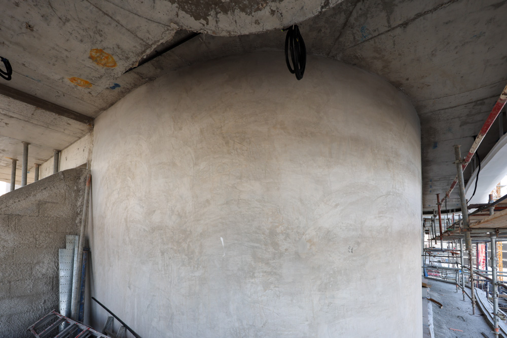 Beach Walk Iii By Imtiaz A partially constructed building interior featuring a large, smooth curved wall and exposed scaffolding.
