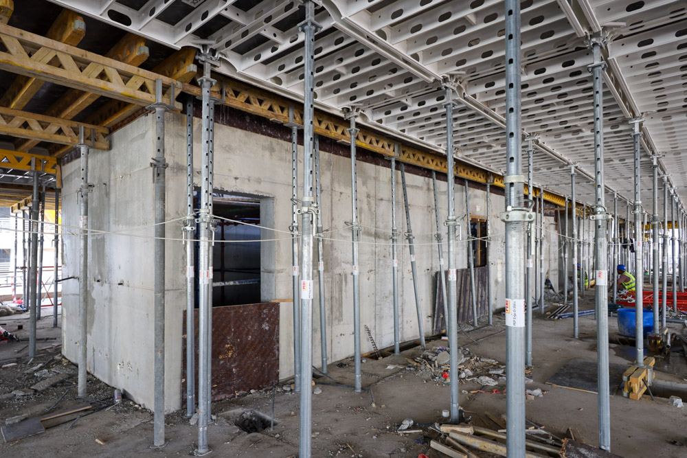Cove Edition I By Imtiaz 1 A construction site featuring concrete walls, scaffolding, and wooden support beams, with scattered materials on the floor.