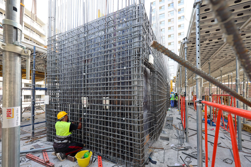 Cove Edition I By Imtiaz 1 A construction site featuring a worker assembling a steel reinforcement structure amidst scaffolding and building materials.