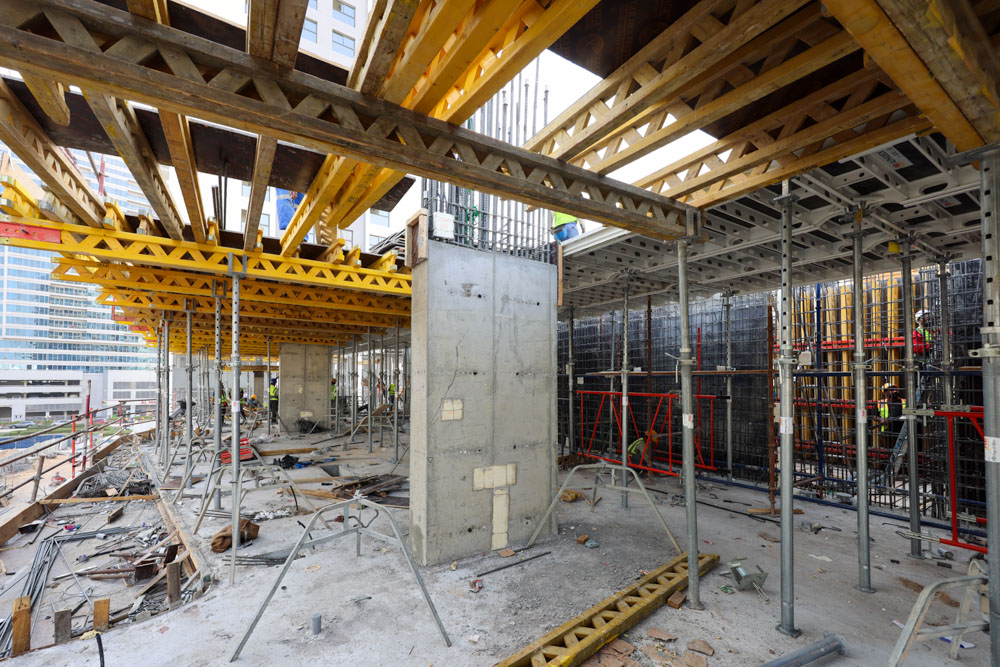 Cove Edition I By Imtiaz 1 Construction site interior featuring scaffolding, wooden beams, and construction workers at various tasks.