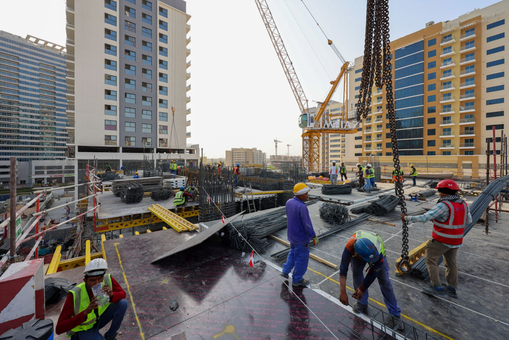 Cove Edition I By Imtiaz 1 Construction site with workers, cranes, and building materials amidst tall buildings under construction.
