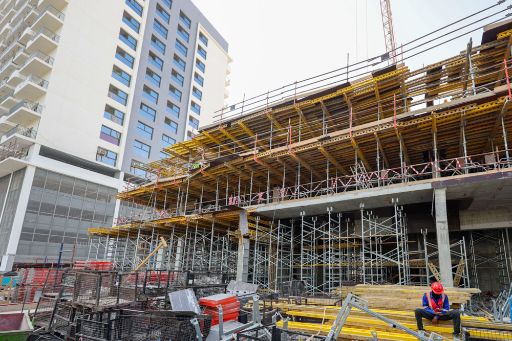 Cove Edition I By Imtiaz 1 Construction site featuring scaffolding, building materials, and a worker in a hard hat sitting on the ground.