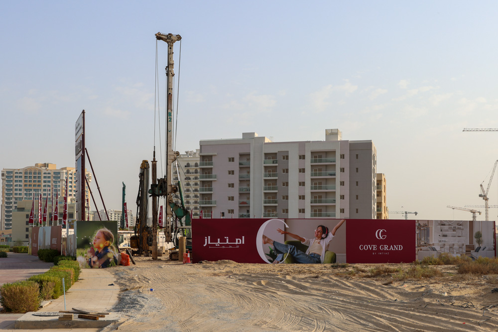 Cove Grand By Imtiaz Construction site featuring drilling equipment, a promotional wall, and modern buildings in the background.
