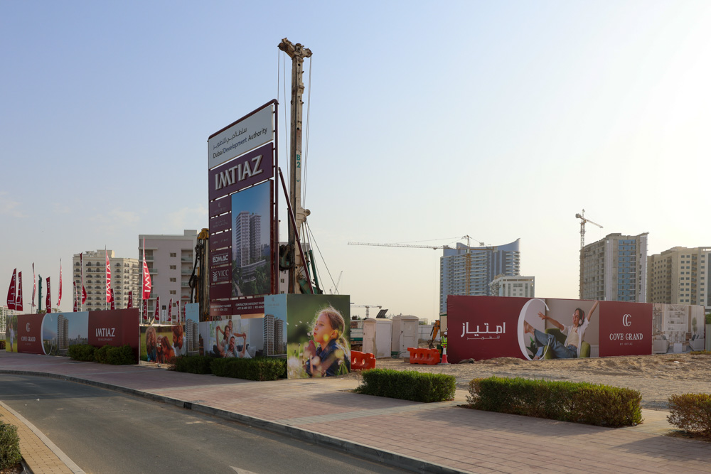 Cove Grand By Imtiaz Construction site showing advertising boards for Imtiaz and Cove Grand, with nearby buildings and cranes in Dubai.
