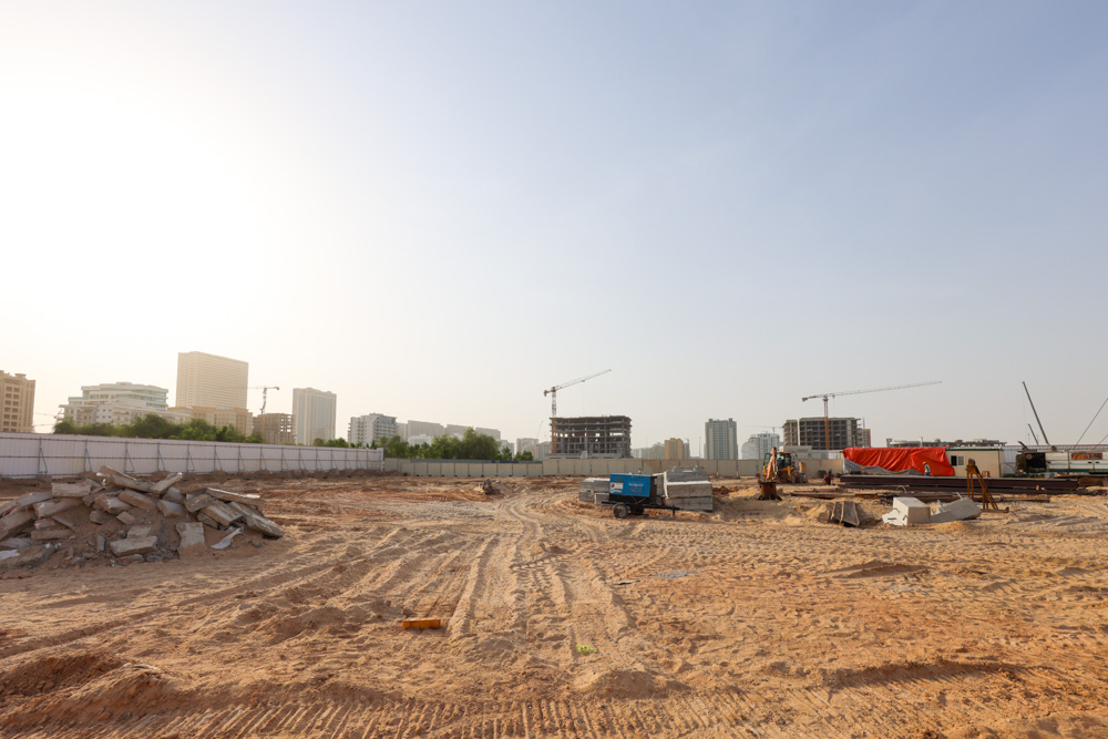 Cove Grand By Imtiaz Construction site with heavy machinery, sand, and piles of debris, surrounded by city buildings and cranes.