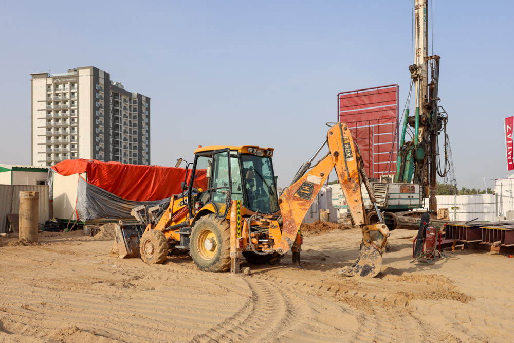 Cove Grand By Imtiaz A construction site featuring a backhoe loader, machinery, and a large building in the background.