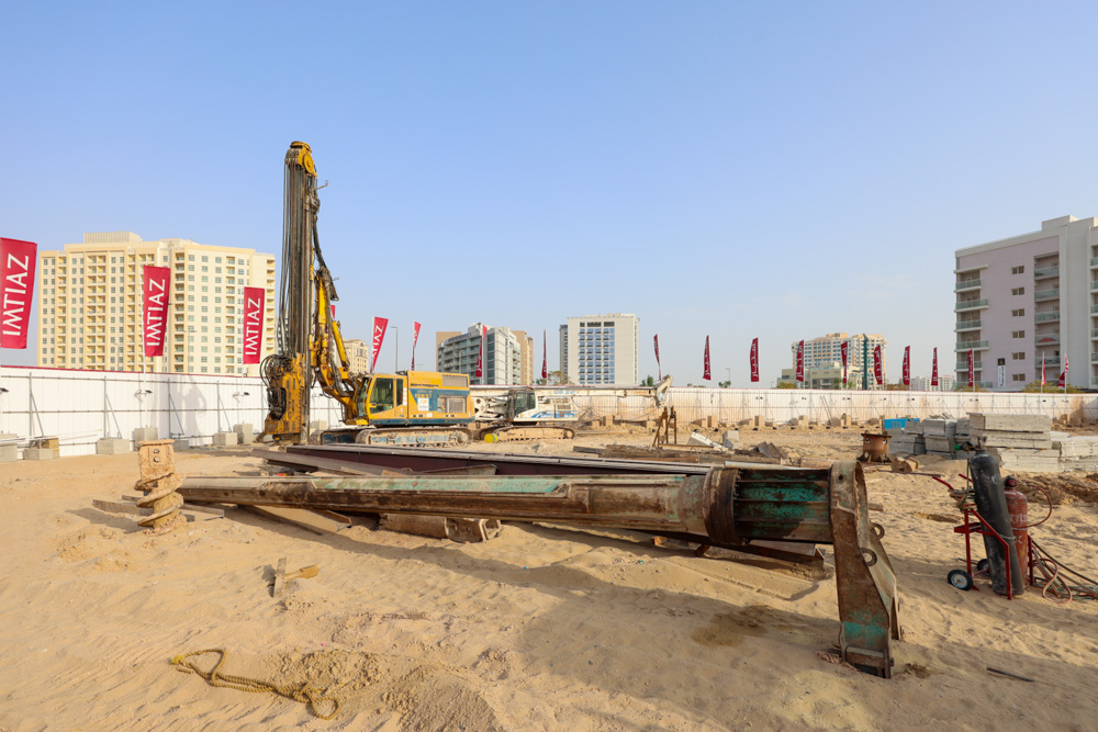 Cove Grand By Imtiaz Construction site with machinery and equipment, including a drilling rig and piled materials, surrounded by buildings.