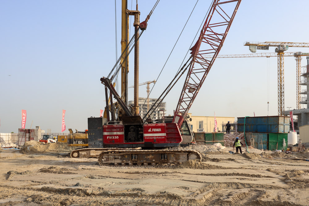 Cotier House 2 By Imtiaz A construction site with a large crane, workers, and various machinery surrounded by piles of sand and materials.
