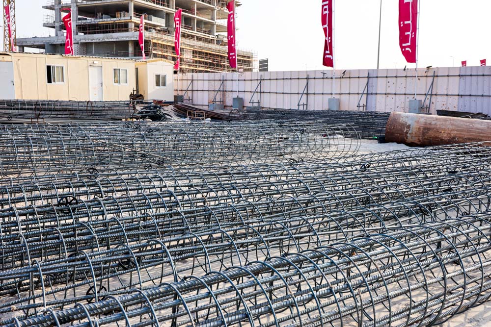 Cotier House 2 By Imtiaz Construction site with stacked rebar, temporary structures, and banners in the background.