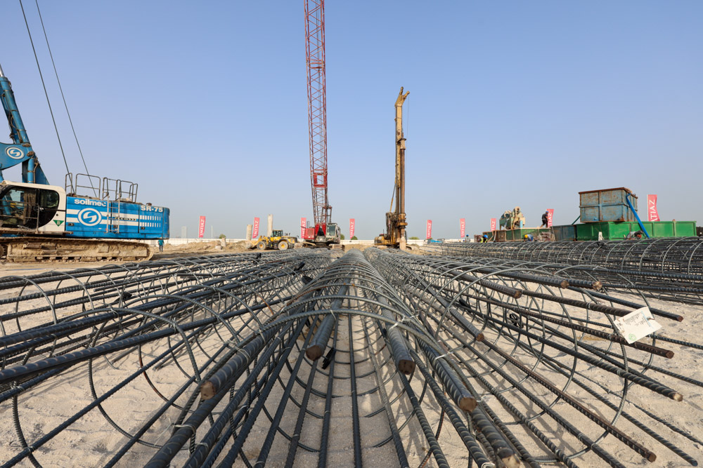 Cotier House 2 By Imtiaz Construction site with machinery and bundled rebar laid out on sandy ground under a clear blue sky.