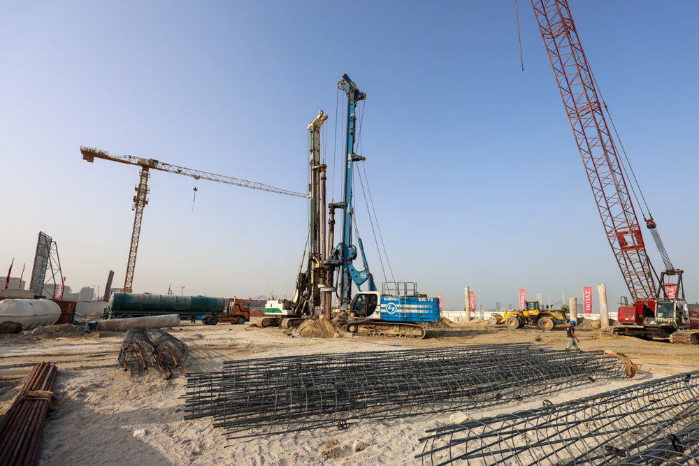 Cotier House 2 By Imtiaz Construction site featuring cranes, machinery, and stacked materials on sandy terrain under a clear blue sky.