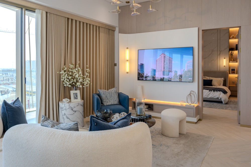 Beach Walk Residence Modern living room with plush seating, a television, and large windows, featuring decorative plants and light curtains.