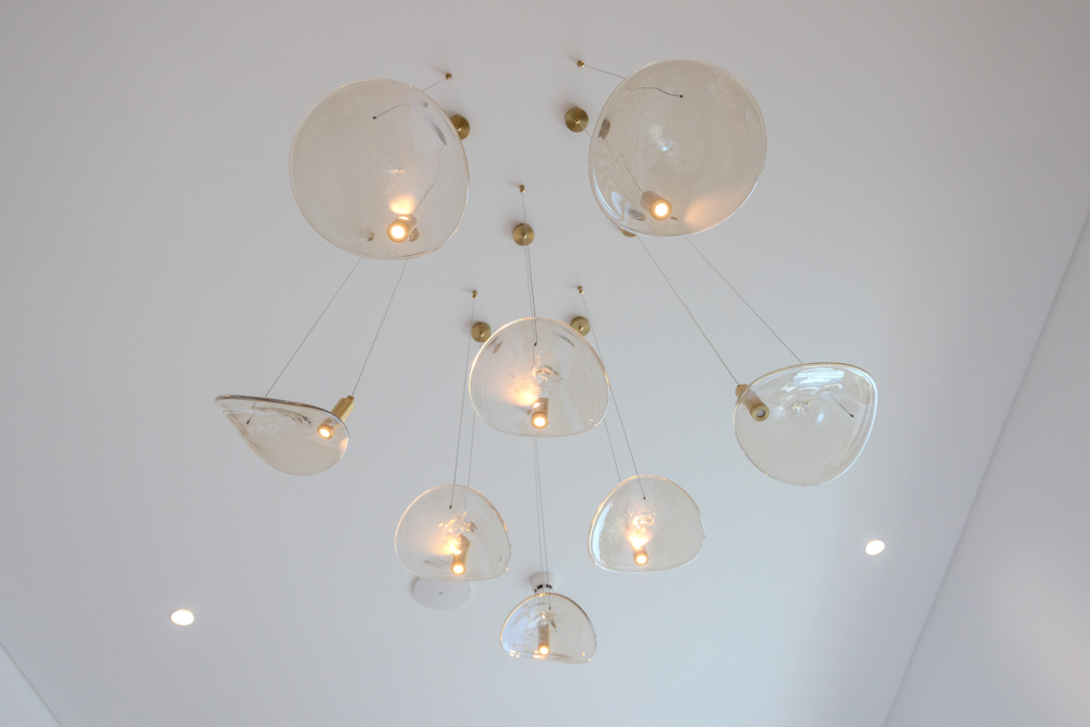 Beach Walk Residence A modern hanging light fixture with multiple clear glass shades, illuminating a minimalist white ceiling.