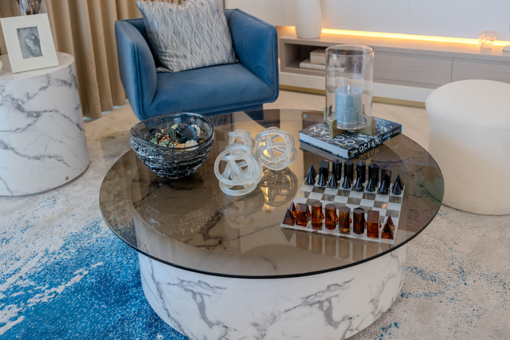 Beach Walk Residence A stylish living room scene featuring a glass coffee table with decorative items, a blue armchair, and soft rug.