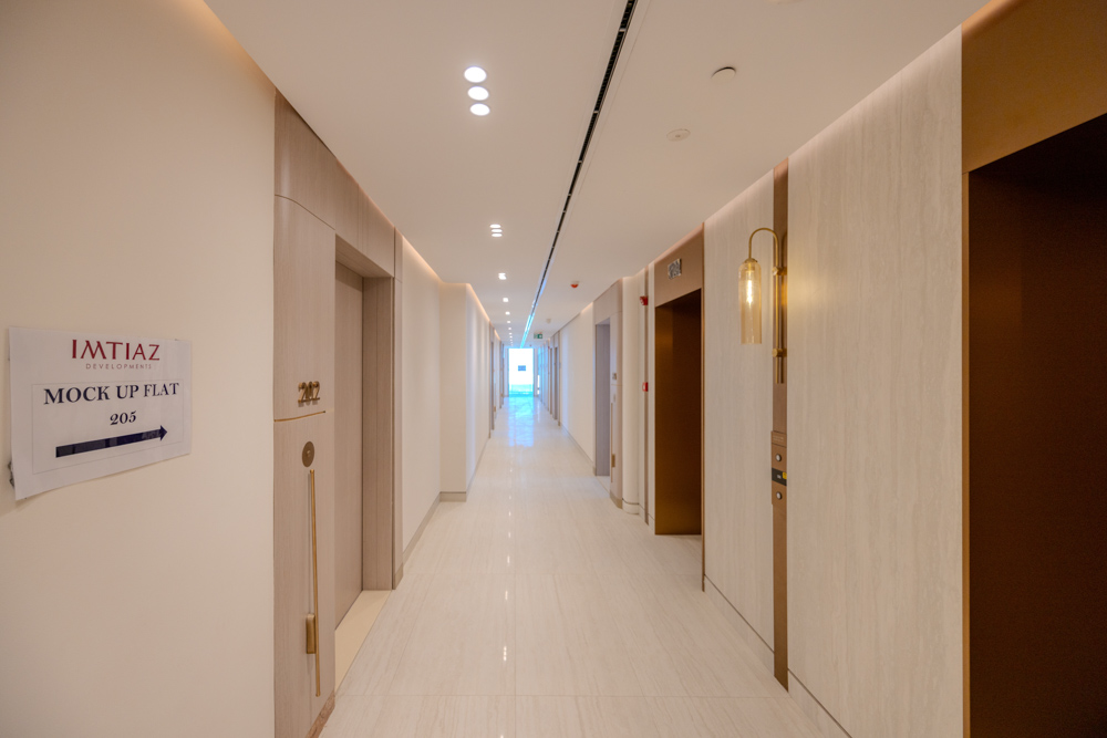 Beach Walk Residence A modern, well-lit hallway featuring several doors, a sign for a mock-up flat, and stylish lighting.