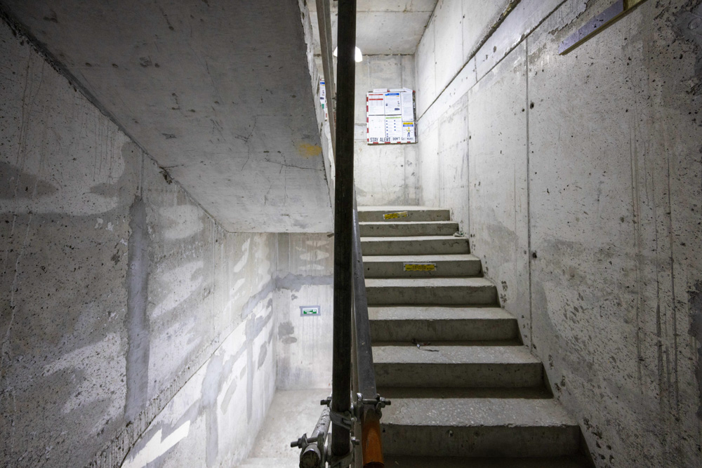 Beach Walk Iii By Imtiaz A concrete stairwell with walls under construction, featuring steps and a poster mounted at the top.