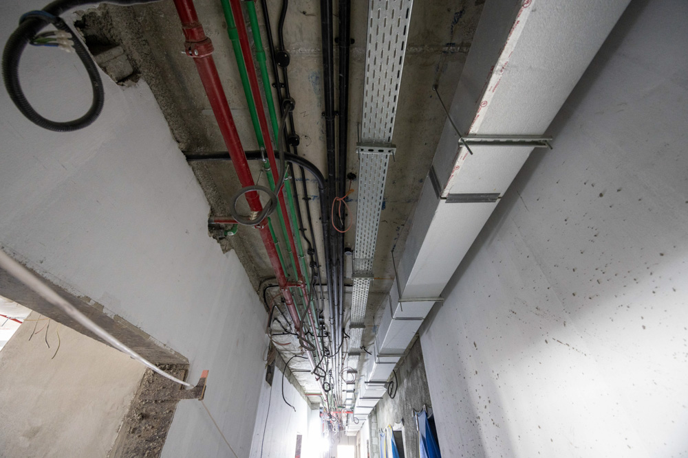 Beach Walk Iii By Imtiaz A view of a construction corridor with exposed pipes, cables, and ductwork along the ceiling.