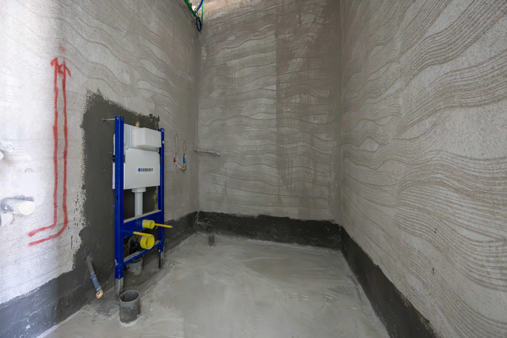Beach Walk Iii By Imtiaz A construction area with plastered walls, a wall-mounted toilet frame, and exposed plumbing fixtures.