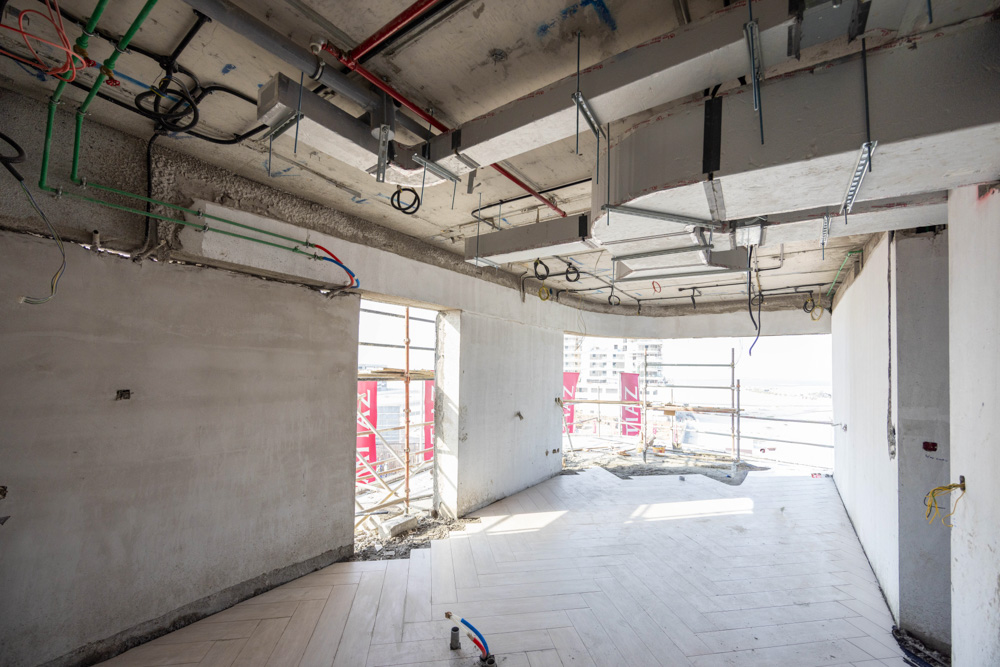 Beach Walk Iii By Imtiaz An unfinished room with exposed walls, ceiling fixtures, and a window revealing a construction site outside.