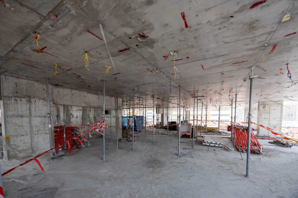 Cove Edition I By Imtiaz 1 An unfinished concrete interior of a building, featuring scaffolding, construction materials, and caution tape.
