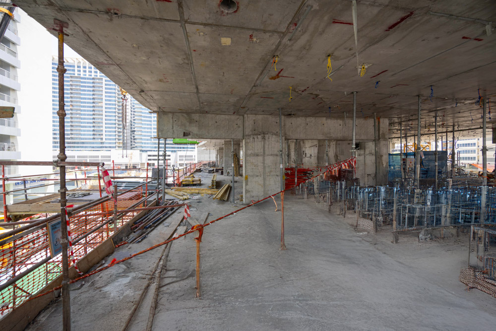 Cove Edition I By Imtiaz 1 Construction site interior showing scaffolding, unfinished concrete floors, and surrounding urban buildings.