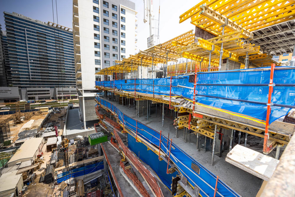 Cove Edition I By Imtiaz 1 Construction site featuring scaffolding, safety barriers, and a partially built high-rise against a city backdrop.