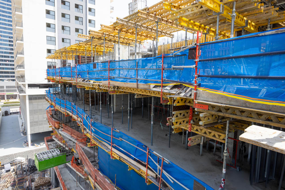 Cove Edition I By Imtiaz 1 A construction site featuring scaffolding, safety netting, and various materials arranged for building a structure.