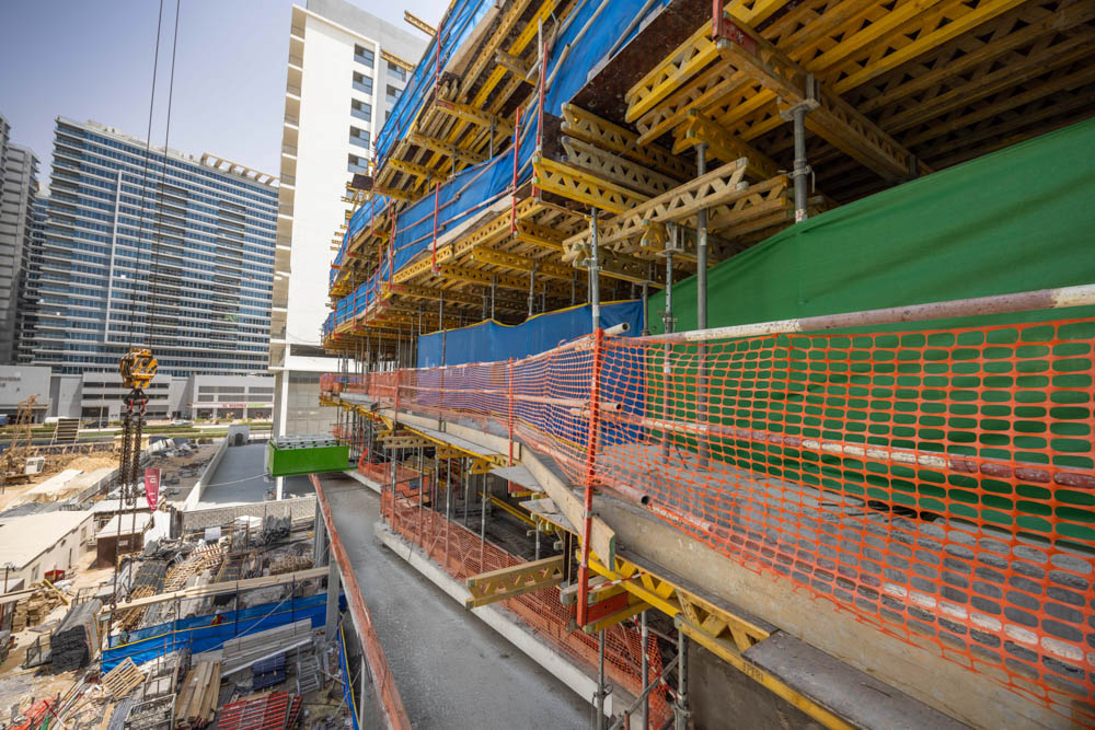 Cove Edition I By Imtiaz 1 Construction site featuring scaffolding, safety nets, and a partially built structure with surrounding buildings.
