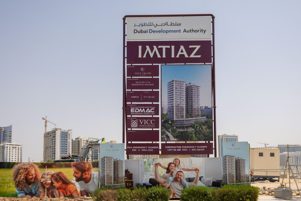 Cove Grand By Imtiaz A large construction sign for IMTIAZ project in Dubai, featuring images of residential buildings and happy families.