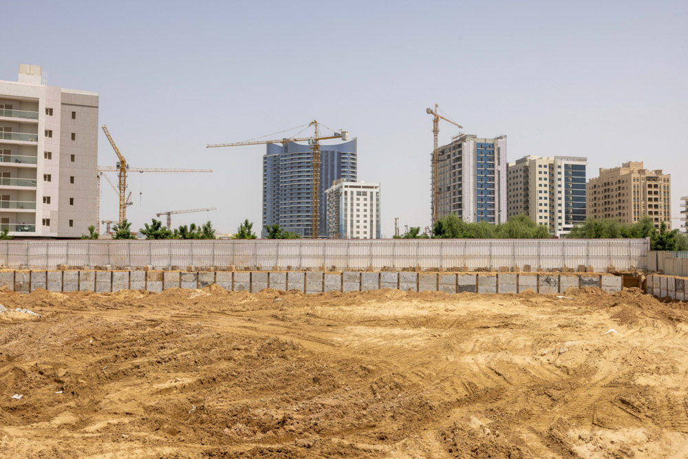 Cove Grand By Imtiaz Construction site with buildings and cranes, featuring a sandy terrain and a fence in the foreground.