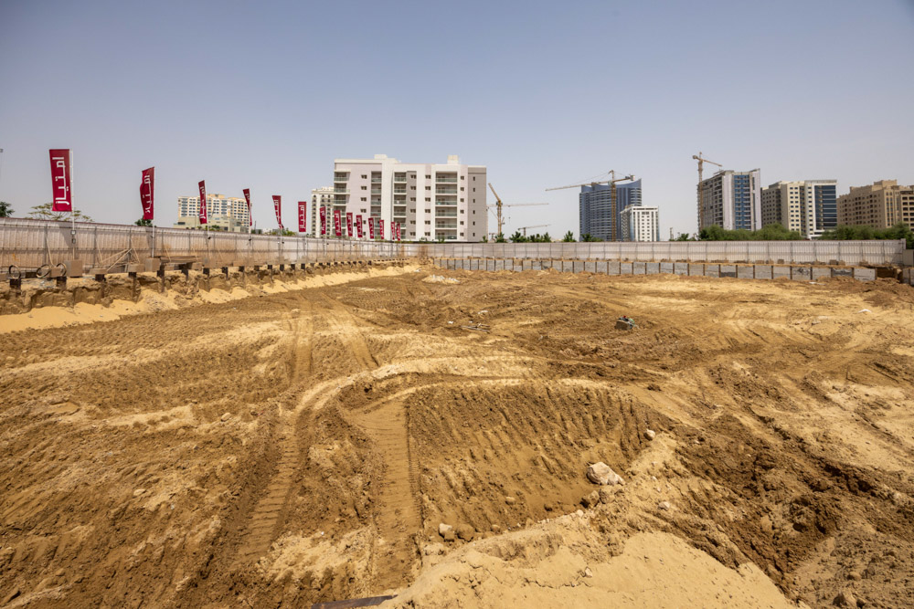 Cove Grand By Imtiaz Construction site with sandy terrain, surrounded by buildings and cranes, and marked by flags along a fence.