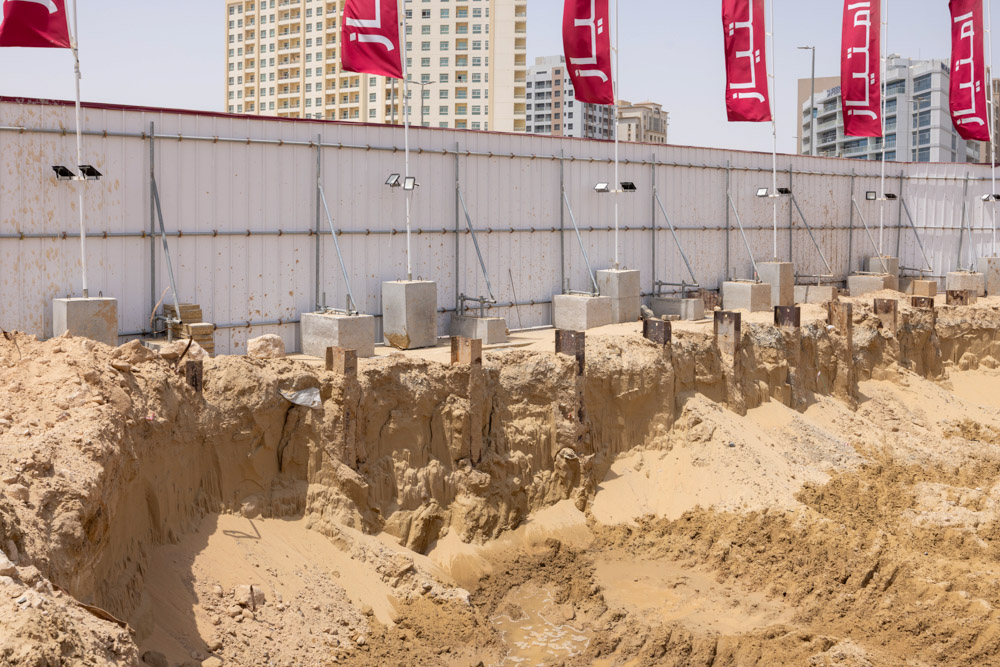 Cove Grand By Imtiaz Excavation site with sandy earth, concrete barriers, and tall buildings in the background under clear skies.