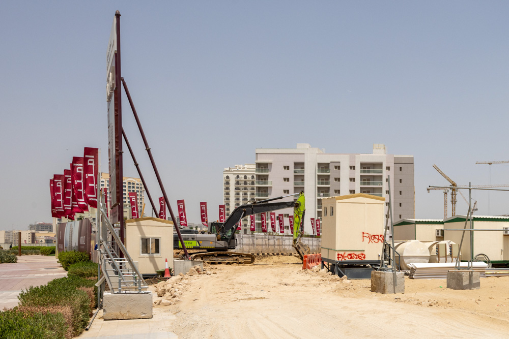Cove Grand By Imtiaz Construction site with machinery, portable buildings, and red flags against a backdrop of modern buildings.