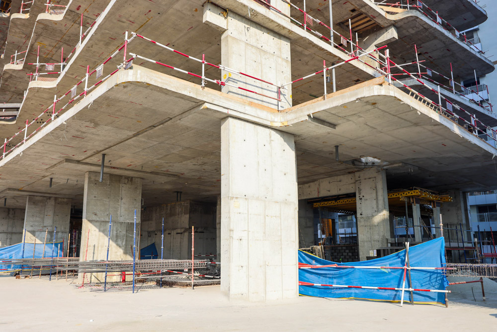Cove Edition I By Imtiaz 1 A construction site featuring concrete pillars, scaffolding, and blue tarps, indicating ongoing building work.