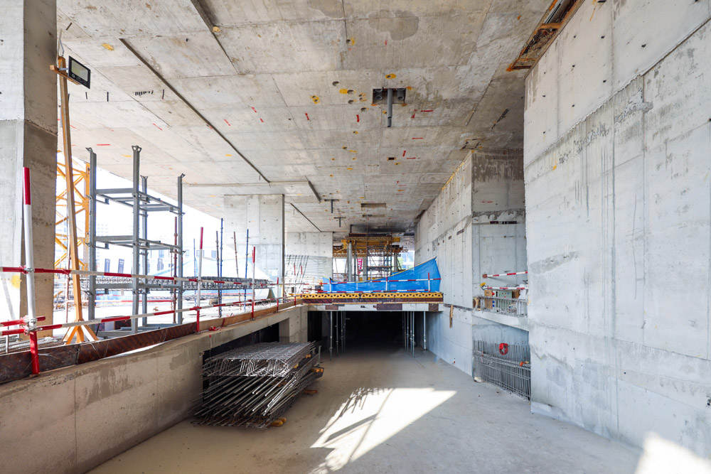 Cove Edition I By Imtiaz 1 An under-construction building interior showcasing concrete walls, scaffolding, and construction materials scattered around.