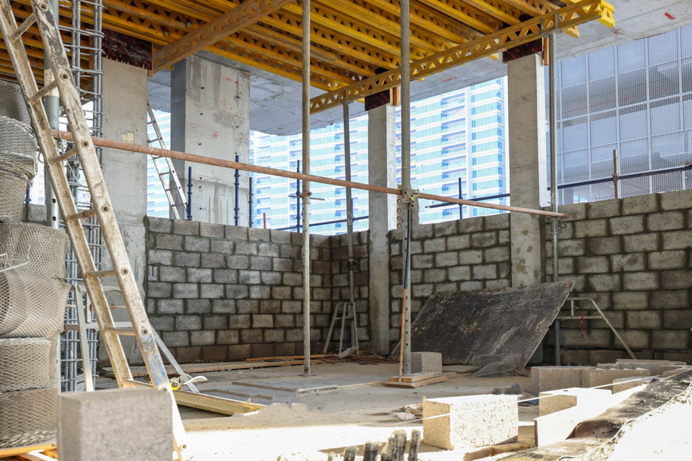 Cove Edition I By Imtiaz 1 Construction site featuring exposed concrete walls, scaffolding, and construction materials scattered on the floor.