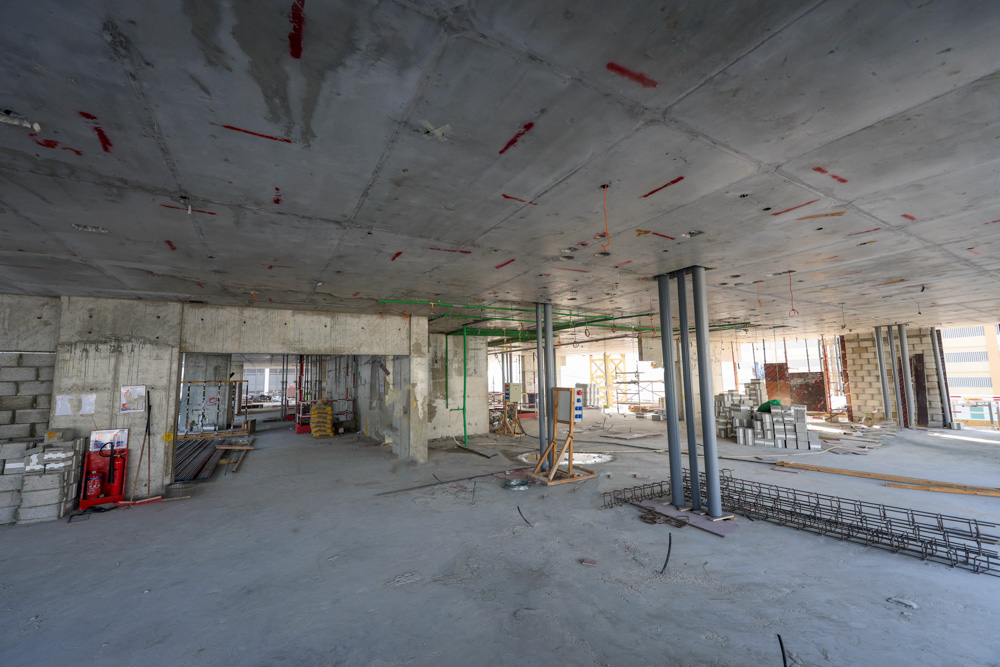 Cove Edition I By Imtiaz 1 Interior of a construction site featuring exposed concrete walls, pillars, scaffolding, and construction materials scattered around.