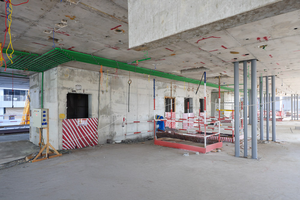 Cove Edition I By Imtiaz 1 An unfinished construction site featuring walls, exposed utilities, and safety barriers in a wide, open space.