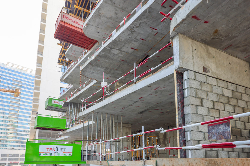 Cove Edition I By Imtiaz 1 Construction site featuring concrete floors, scaffolding, and green lift equipment, with a modern building backdrop.